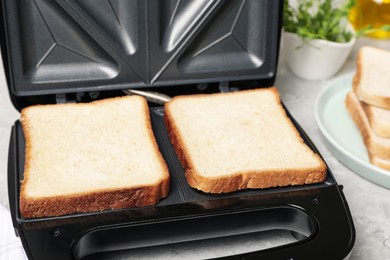 Photo of Modern sandwich maker with bread slices on light grey table, closeup