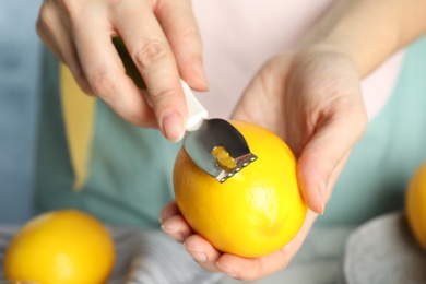 Woman zesting fresh lemon indoors, closeup view