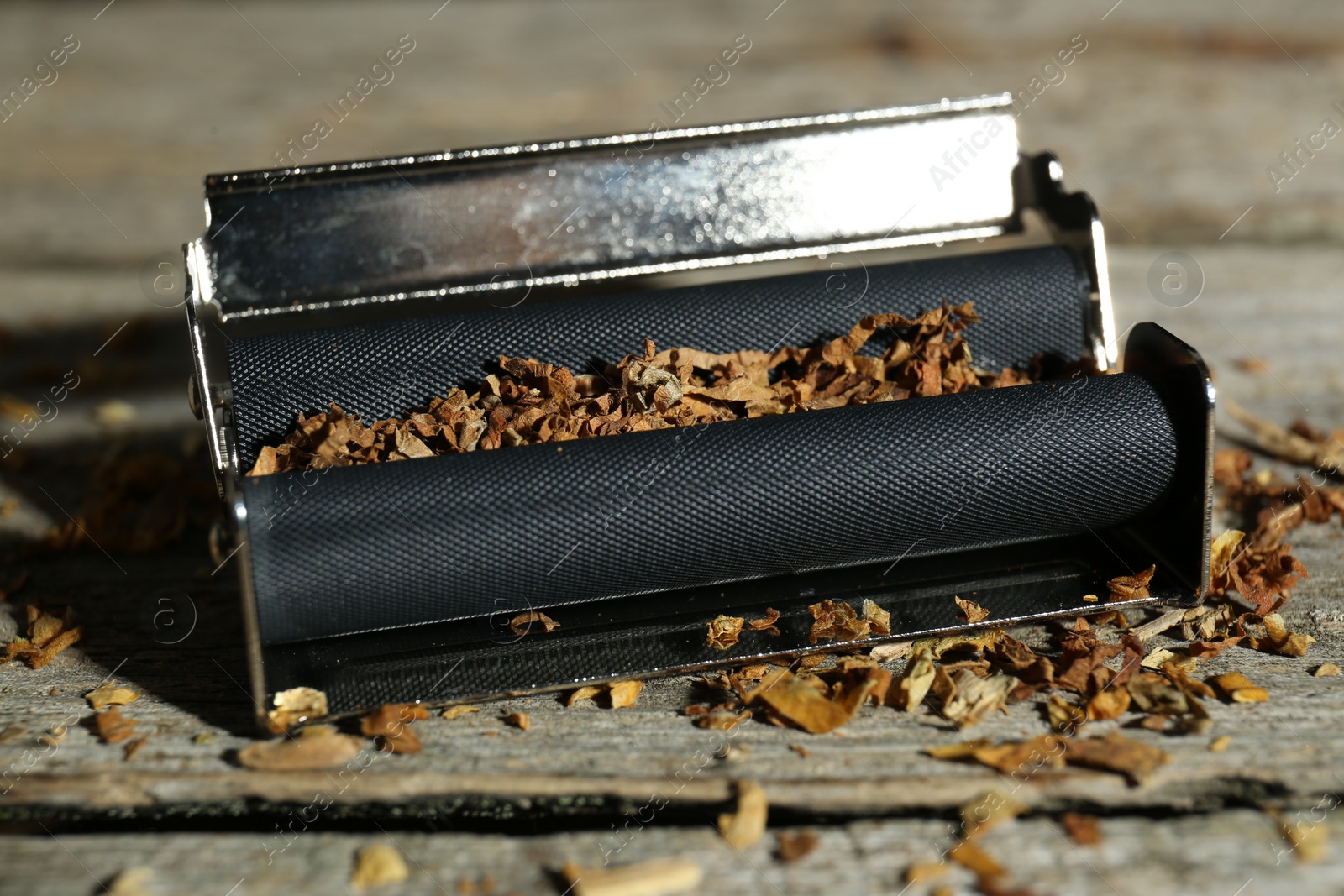 Photo of Roller with tobacco on old wooden table, closeup. Making hand rolled cigarettes