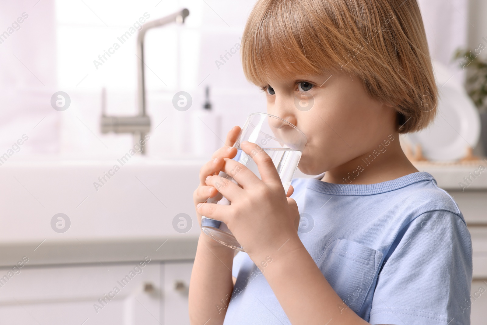 Photo of Cute little boy drinking fresh water from glass at home. Space for text