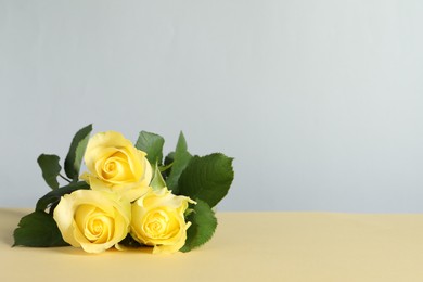 Photo of Beautiful fresh yellow roses on beige table against light grey background. Space for text