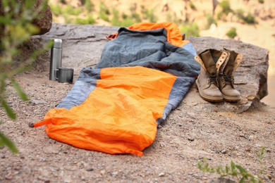 Sleeping bag, thermos and boots outdoors on sunny day