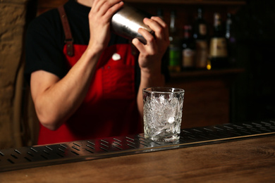 Bartender preparing fresh alcoholic cocktail at bar counter, focus on glass