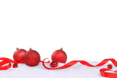 Photo of Beautiful red Christmas balls, ribbon and sleigh bells on snow against white background