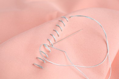 Photo of Sewing needle with thread and stitches on coral cloth, closeup