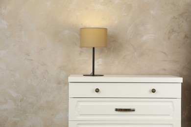 Photo of Modern chest of drawers with lamp near beige wall. Space for text