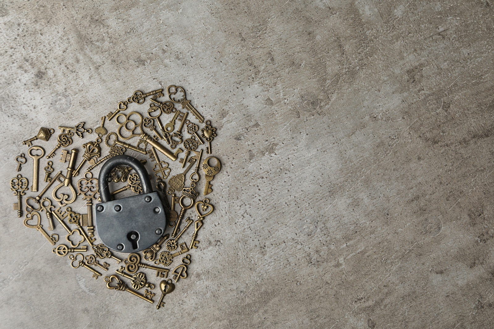 Photo of Heart made of keys, steel padlock and space for text on light stone background, top view. Safety concept