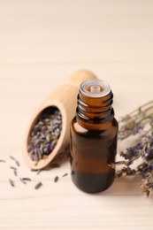 Bottle of essential oil and lavender flowers on white wooden table, closeup