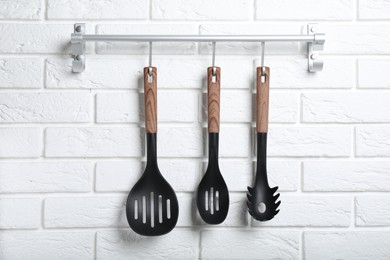 Rack with kitchen utensils hanging on white brick wall