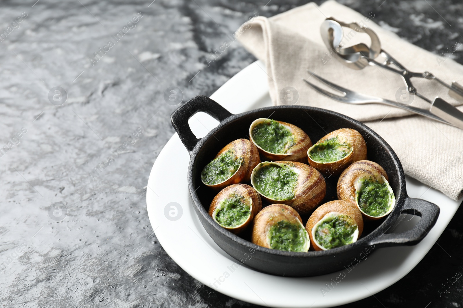 Photo of Delicious cooked snails in baking dish served on grey textured table. Space for text