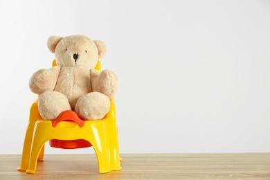 Photo of Teddy bear with yellow potty on wooden table against light background, space for text. Toilet training