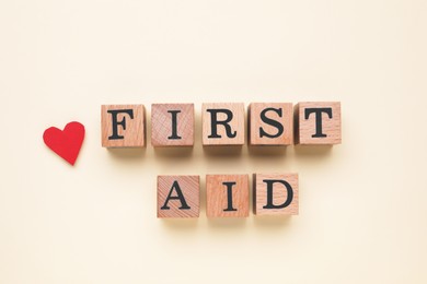 Words First Aid made of wooden cubes and cardboard heart on beige background, flat lay