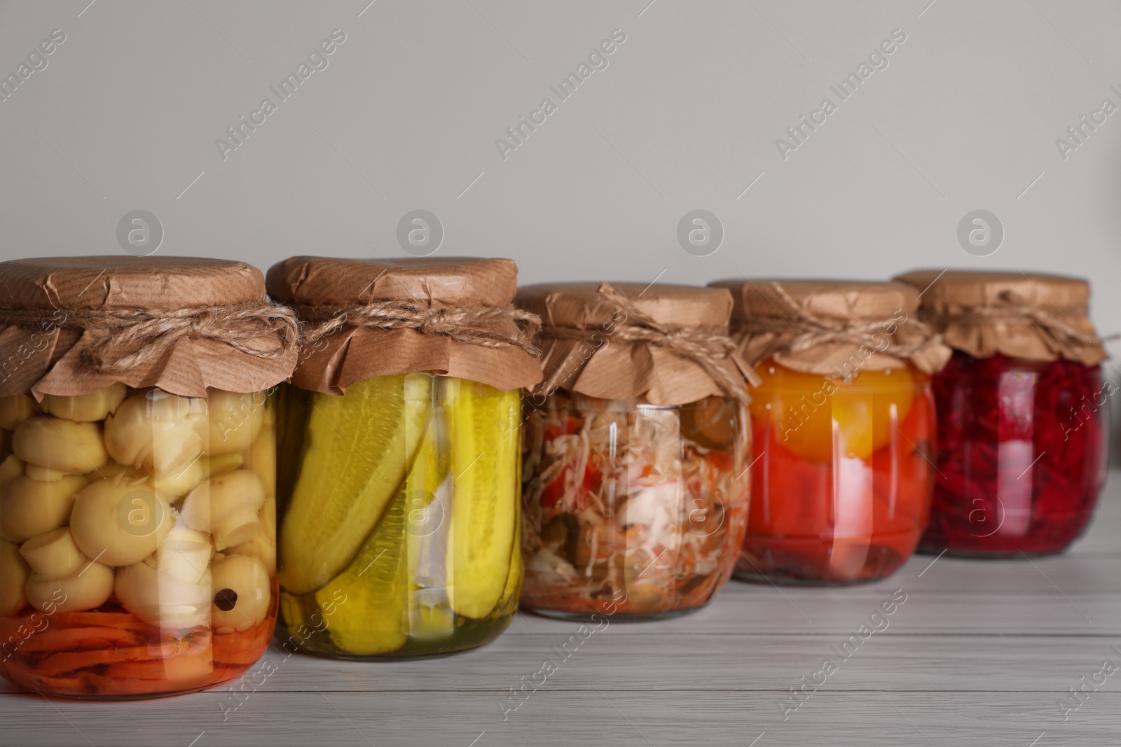 Photo of Many jars with preserved vegetables on white wooden table