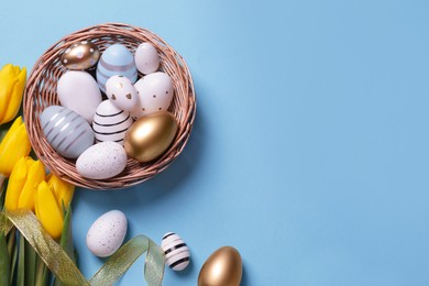 Photo of Many painted Easter eggs, tulip flowers and ribbon on light blue background, flat lay. Space for text