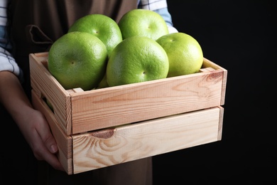 Woman holding wooden crate with sweetie fruits on black background, closeup