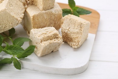 Pieces of tasty halva and mint on white wooden table, closeup