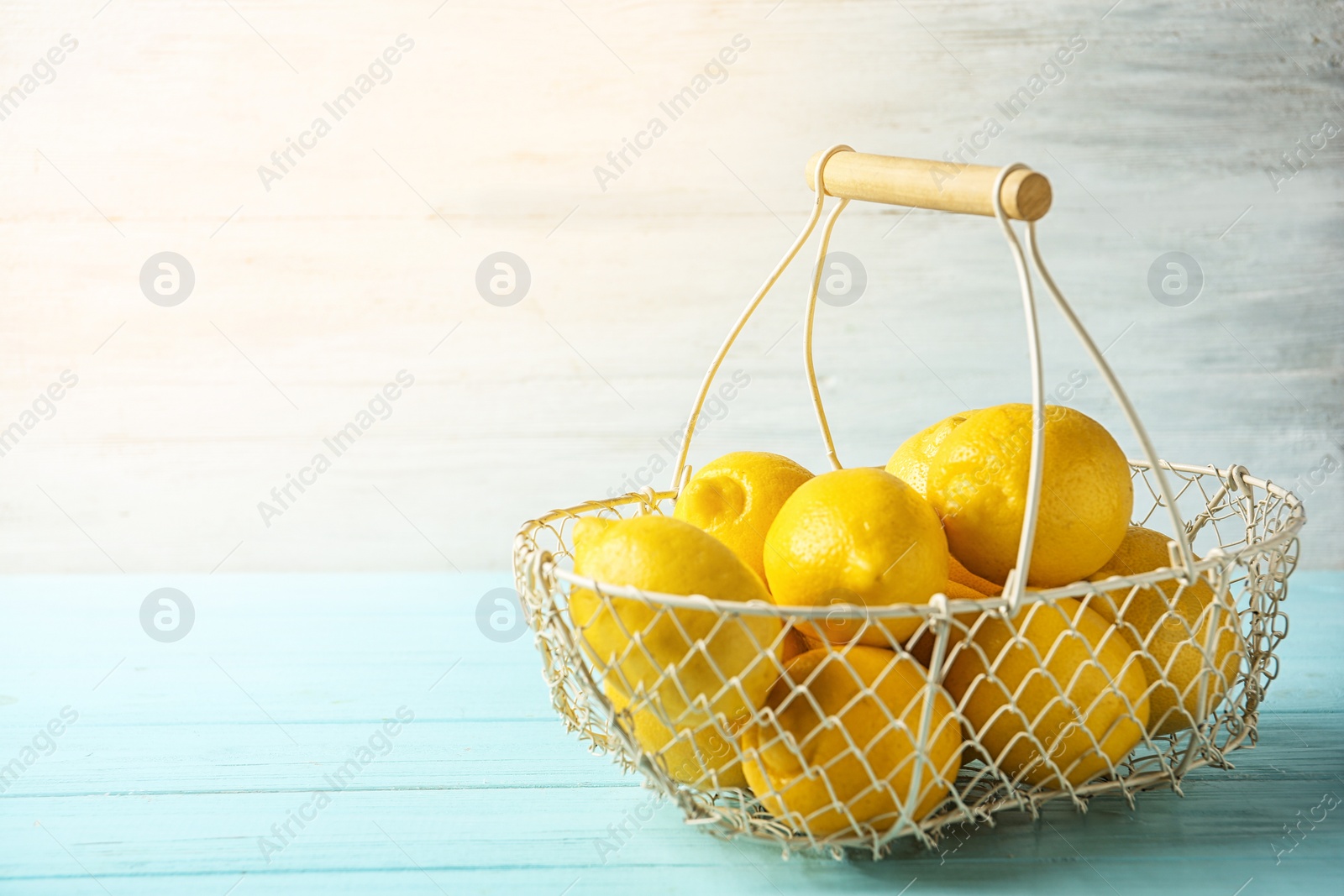 Photo of Basket with ripe lemons on table against light background