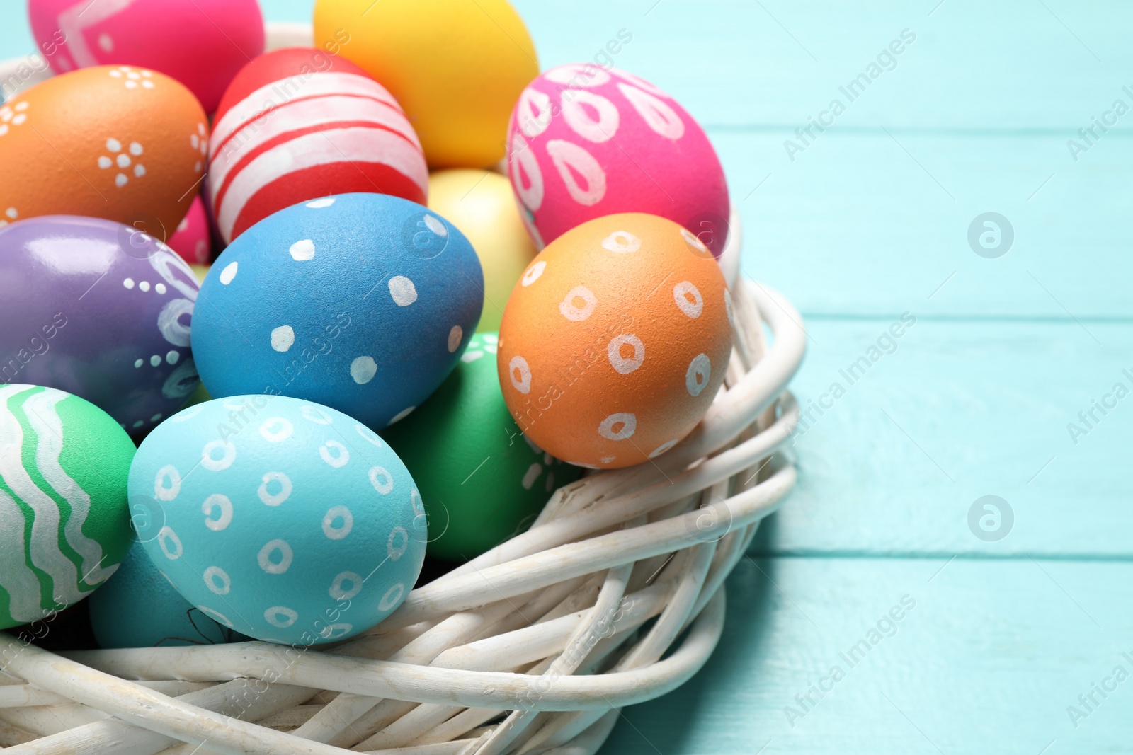 Photo of Colorful Easter eggs in decorative nest on light blue wooden background, closeup