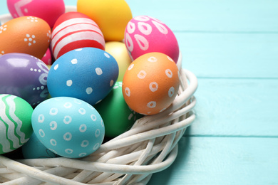 Colorful Easter eggs in decorative nest on light blue wooden background, closeup