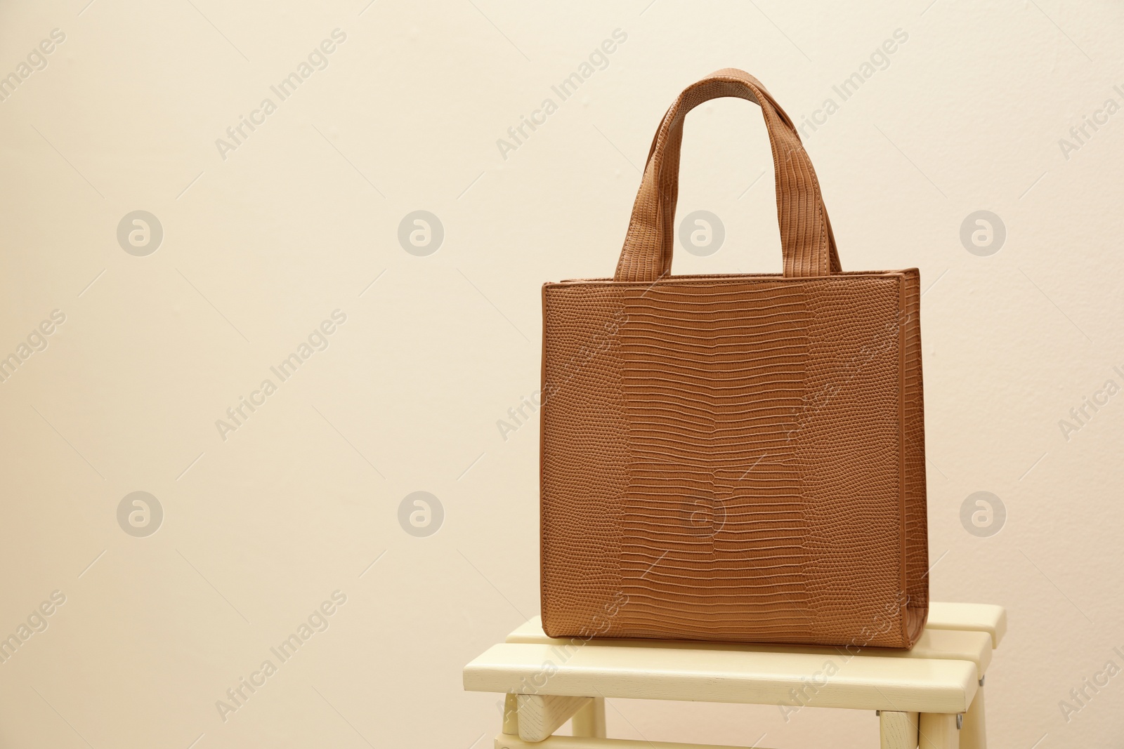 Photo of Stylish woman's bag on wooden stand near beige wall. Space for text