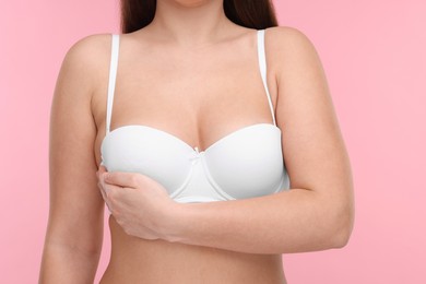 Photo of Mammology. Woman in bra doing breast self-examination on pink background, closeup