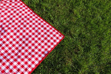 Checkered picnic tablecloth on fresh green grass, top view. Space for text