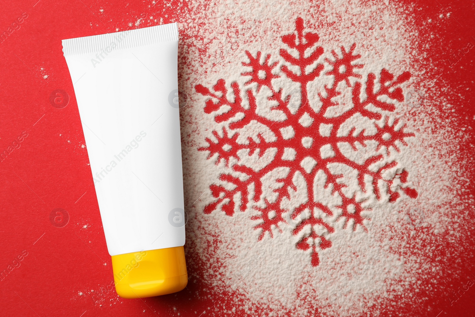 Winter skin care. Hand cream and snowflake silhouette made with artificial snow on red background, top view Photo of Winter skin care. Hand cream and snowflake silhouette made with artificial snow on red background, top view