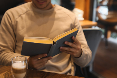 Man with coffee reading book at wooden table, closeup