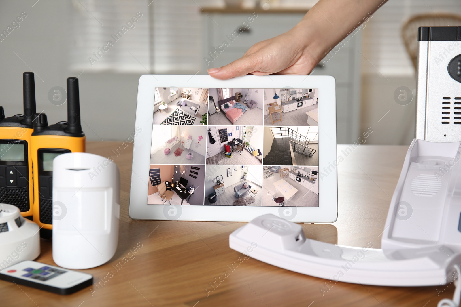 Photo of Woman monitoring CCTV cameras on tablet at wooden table indoors, closeup. Home security system