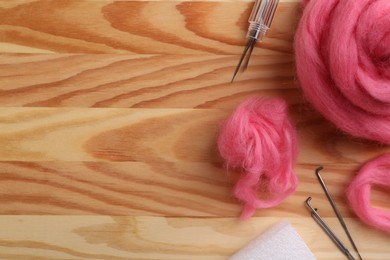 Photo of Pink felting wool and needles on wooden table, flat lay. Space for text
