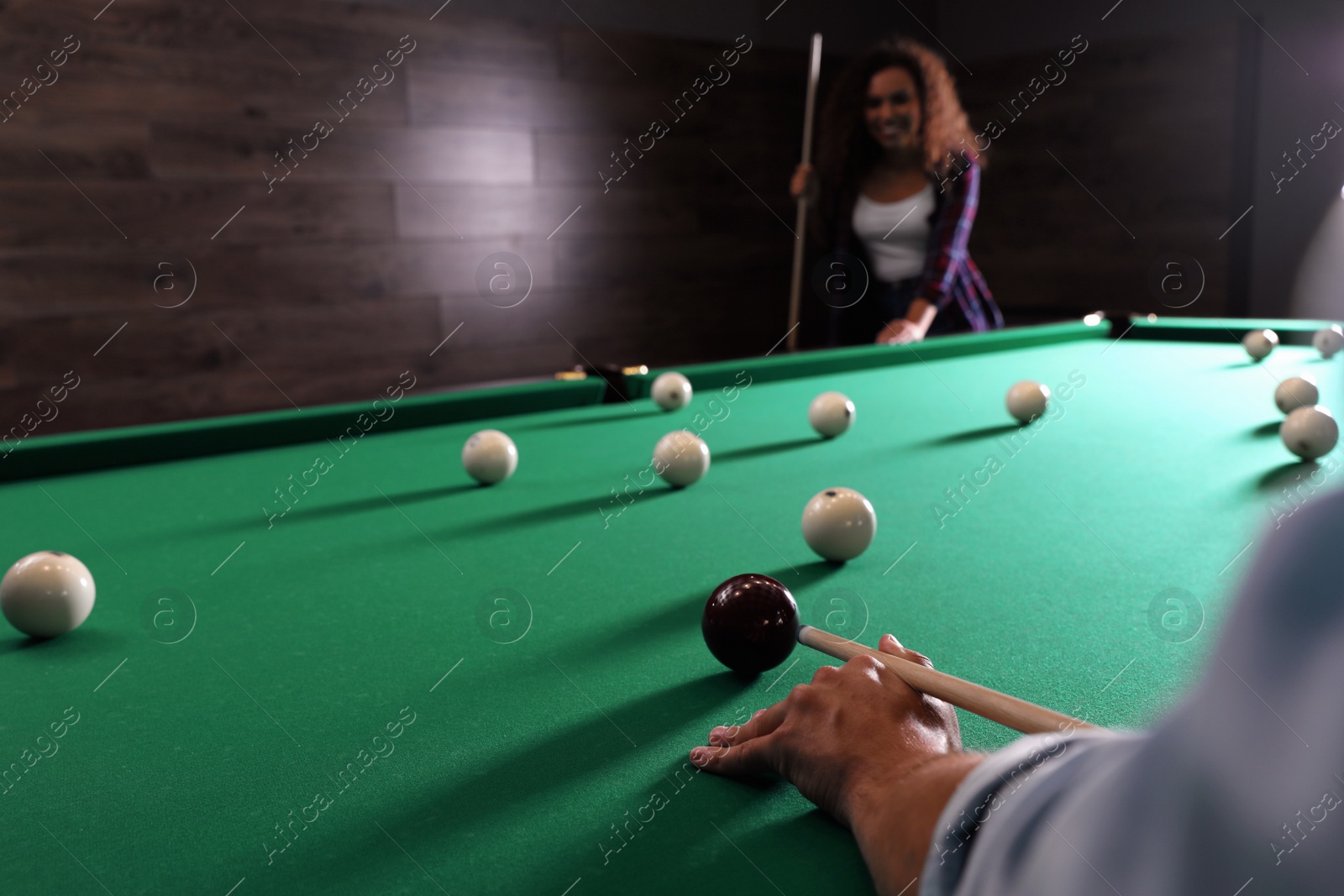 Photo of Young man playing billiard and blurred African-American woman on background, closeup. Space for text