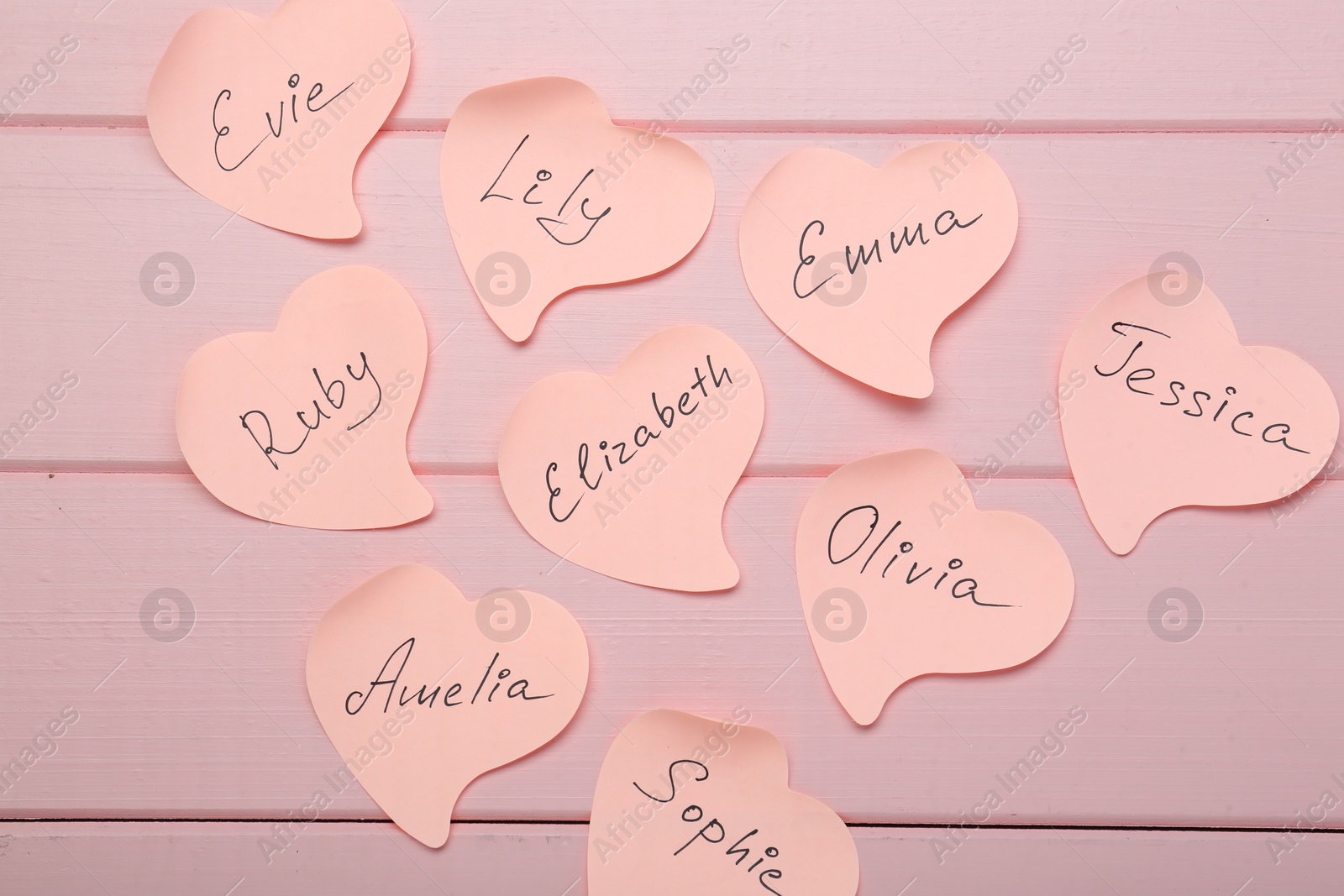 Photo of Paper stickers with different names on pink wooden background, flat lay. Choosing baby's name