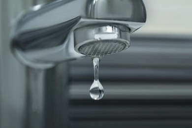 Photo of Water drop falling down from tap on blurred background, closeup