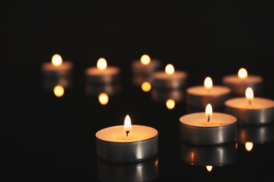 Photo of Many burning candles on black table in darkness