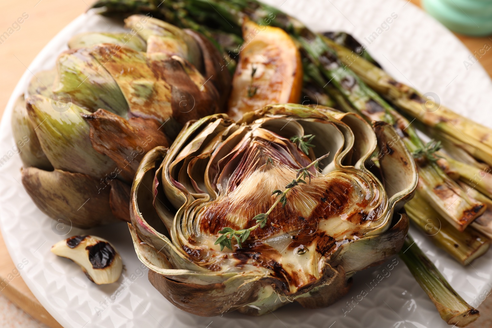 Photo of Plate with tasty grilled artichokes and asparagus on table, closeup