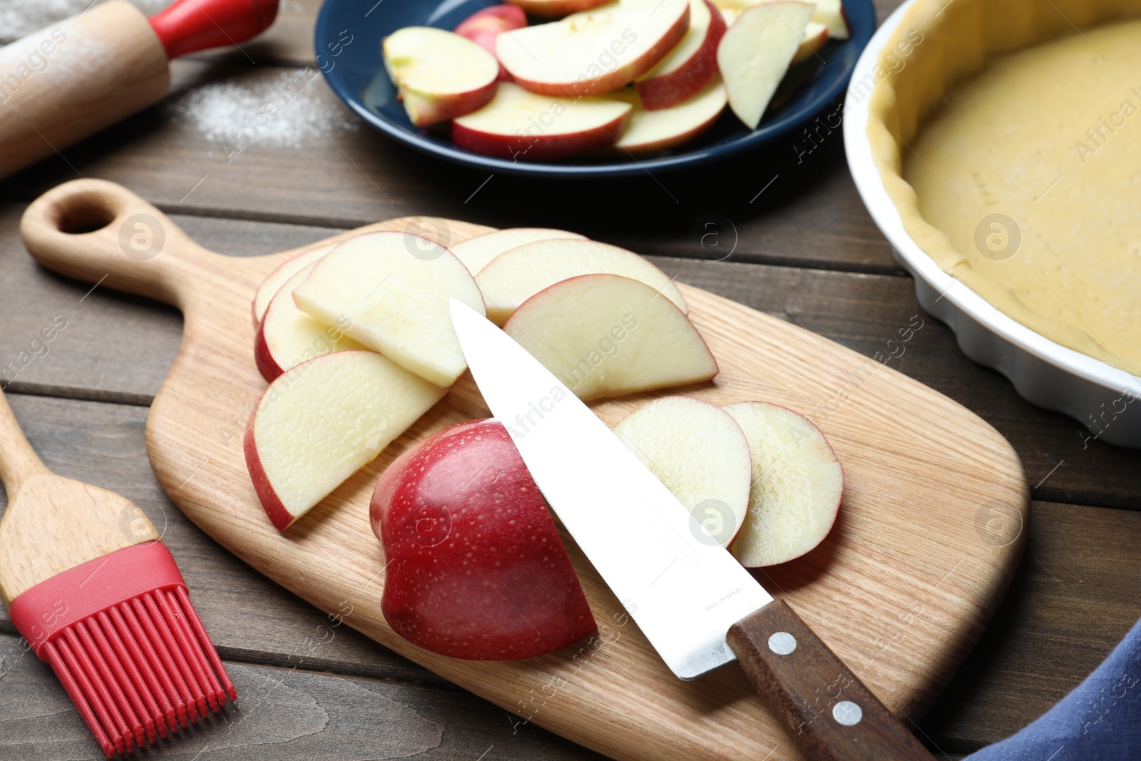 Photo of Cut fresh apple with knife and board on wooden table. Baking pie