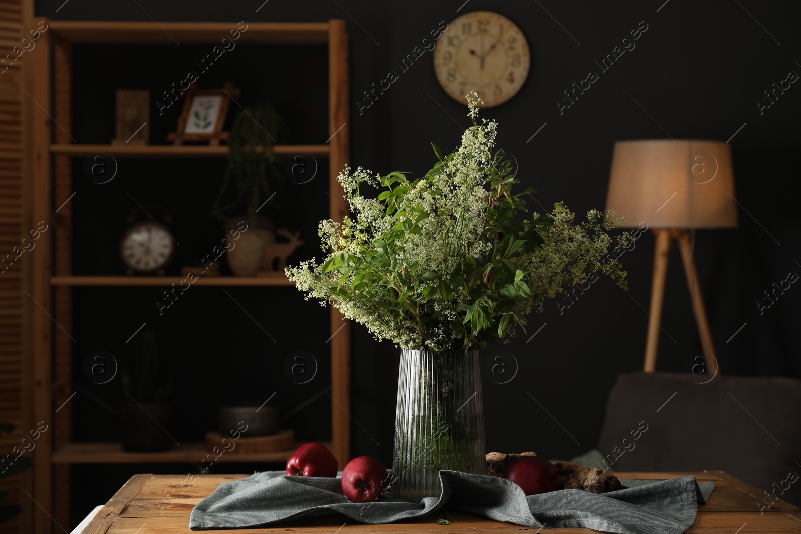 Photo of Ripe red apples and flowers on wooden table in stylish dining room