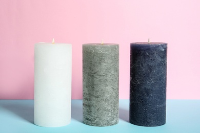 Photo of Decorative wax candles on table against color background