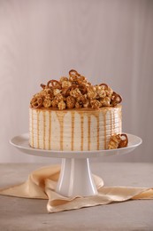 Photo of Caramel drip cake decorated with popcorn and pretzels on light grey table