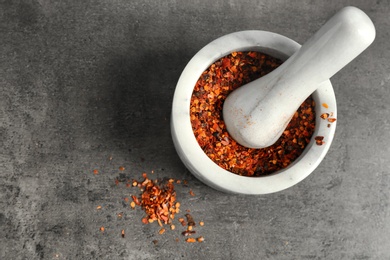 Ceramic mortar with chili pepper flakes on grey background, top view