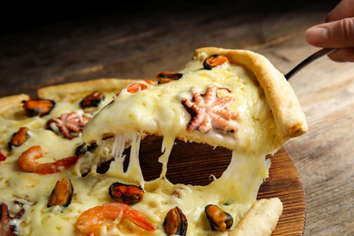 Woman taking piece of delicious seafood pizza at wooden table, closeup