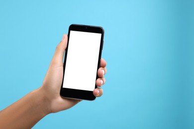 Man holding smartphone with blank screen on light blue background, closeup. Mockup for design