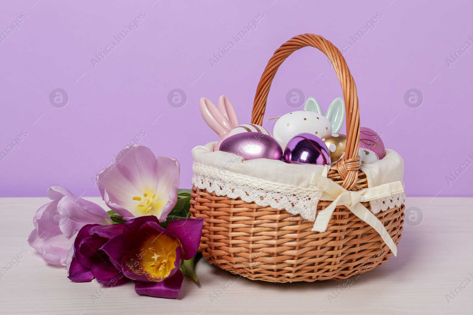 Photo of Easter basket with painted eggs, decorations and flowers on white wooden table