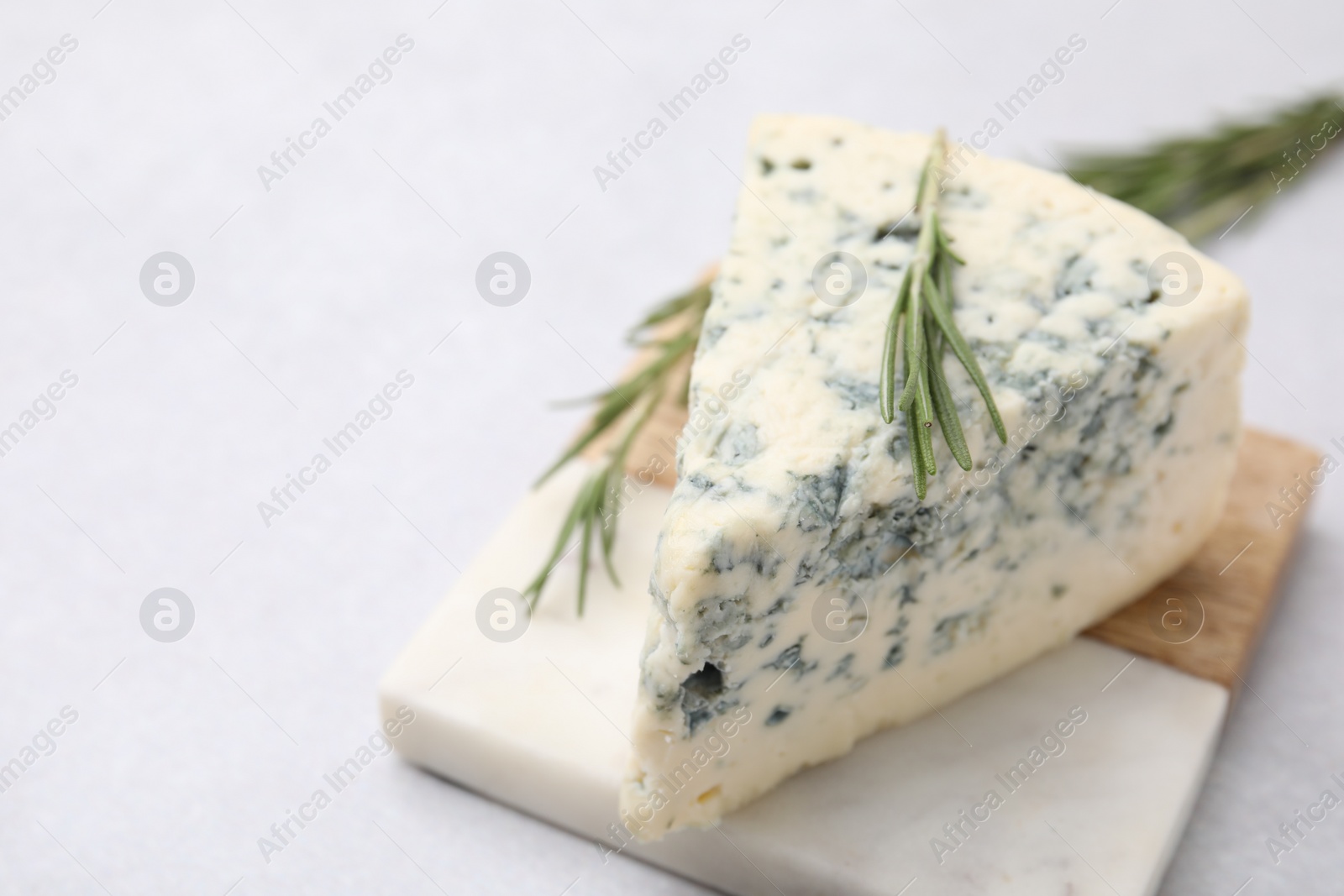 Photo of Tasty blue cheese with rosemary on light table, closeup. Space for text