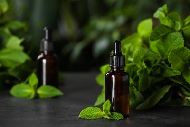 Photo of Bottle of mint essential oil and green leaves on grey table, space for text
