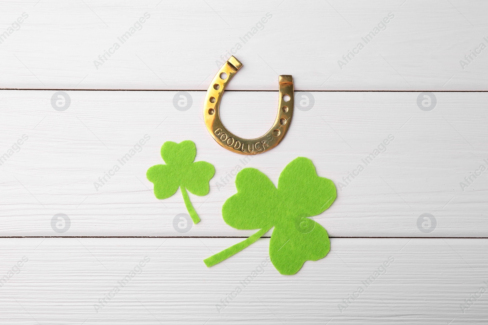 Photo of St. Patrick's day. Golden horseshoe and green decorative clover leaves on white wooden table, flat lay