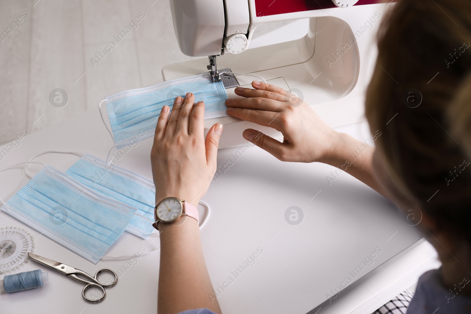 Photo of Woman sewing disposable protective mask with machine at table, closeup