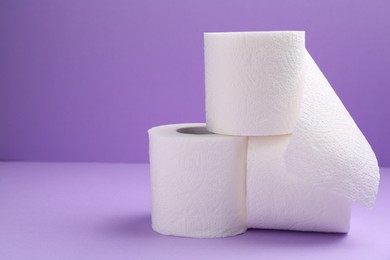 Photo of Soft toilet paper rolls on violet background, closeup. Space for text