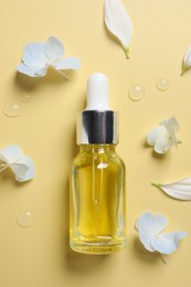 Bottle of cosmetic serum and beautiful flowers on pale yellow background, flat lay
