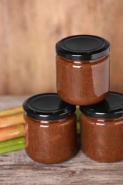 Photo of Jars of tasty rhubarb jam on wooden table, closeup